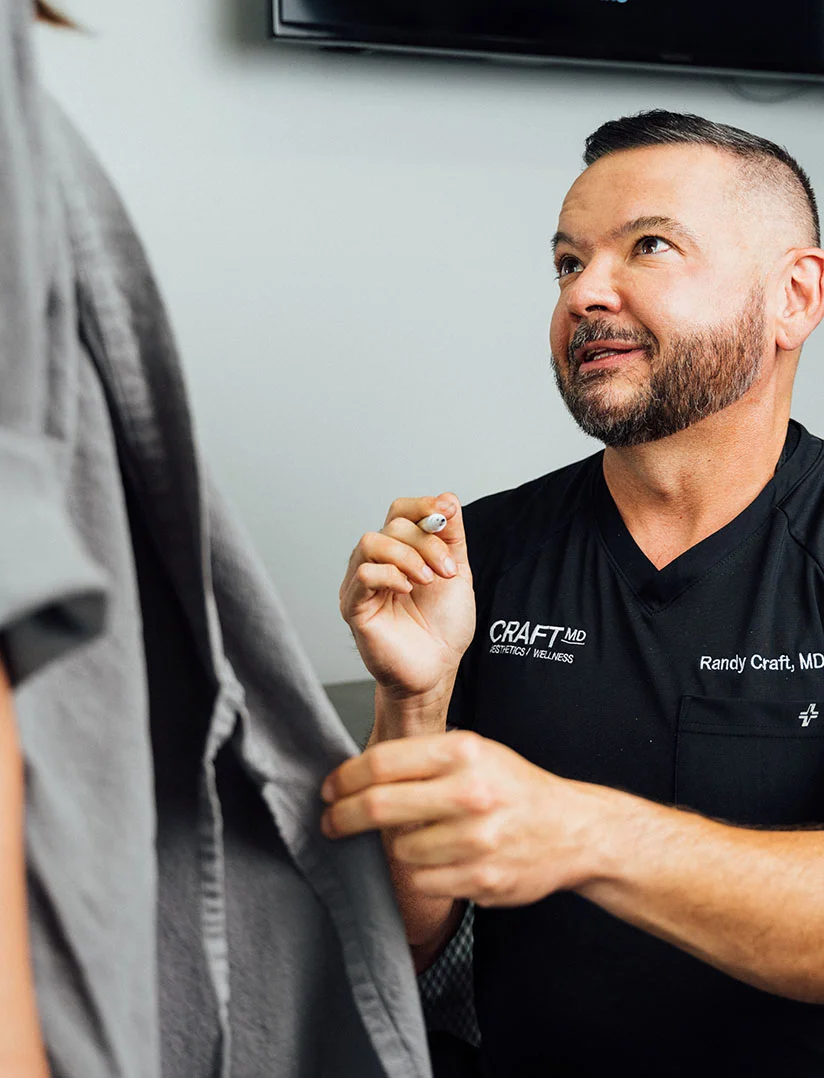 Close up shot of Dr. Craft in a consultation with a client. The client is seen slightly in the shot standing wearing a grey robe. - Body Lift in Phoenix, AZ