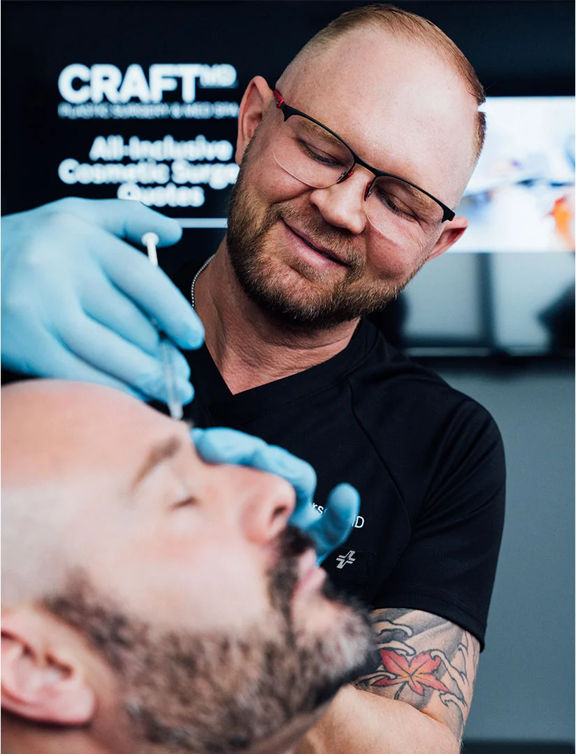 A close up shot of Dr. Craft giving a male client botox above his eyebrow. Dr. Craft is seen smiling while gently giving the shot. - Botox for Men in Phoenix, AZ